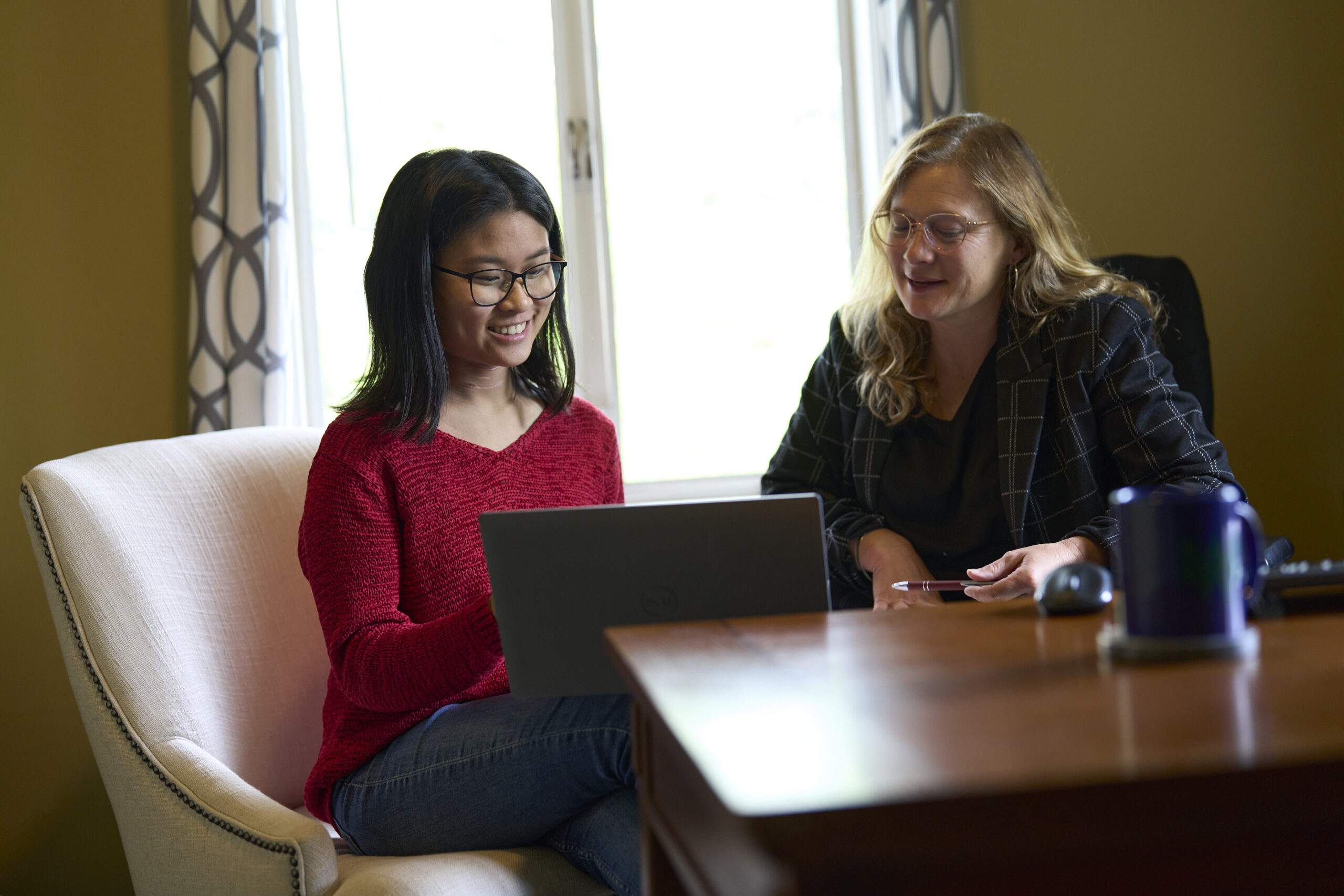 Sophia Huang works hands-on with Amy Ager on a project at the computer. They are smiling and speaking with one another.